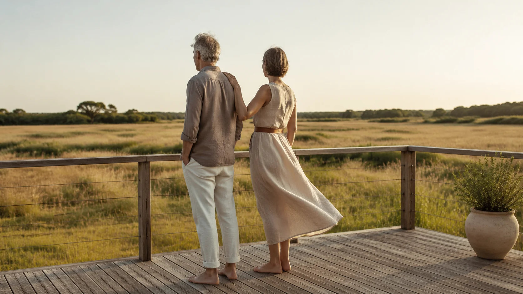 Older couple walking barefoot together on a wooden deck overlooking a meadow, candid editorial lifestyle, soft daylight.