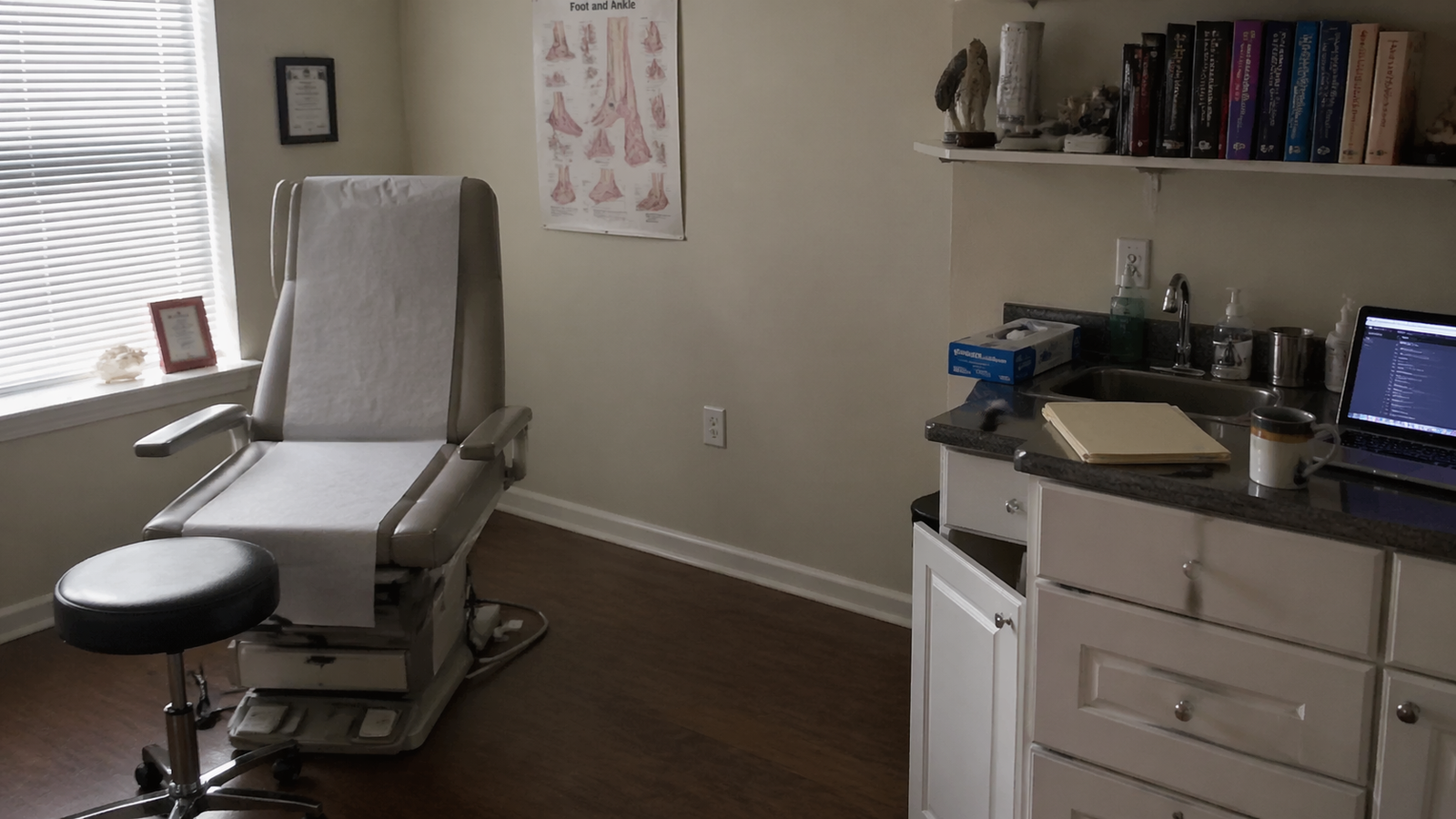 Empty podiatrist exam room at end of day, late afternoon golden light through venetian blinds.