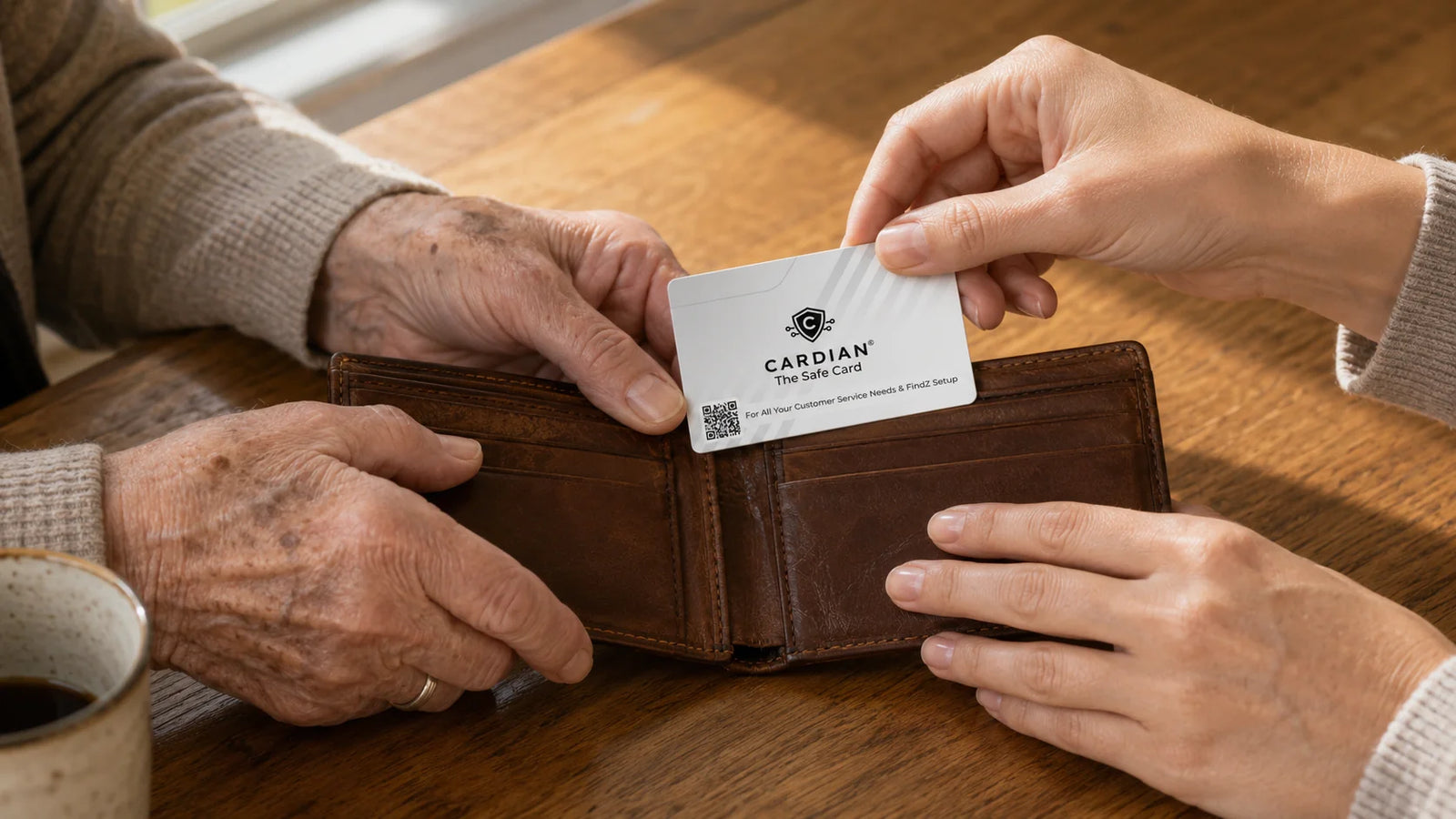 Closeup of two pairs of hands at a warm oak kitchen table — an older mother's hand holds an open worn leather wallet, while her adult daughter's hand holds a real Cardian card (white with grey diagonal stripes, black shield, QR code) mid-air about to slip it into the wallet's card slot