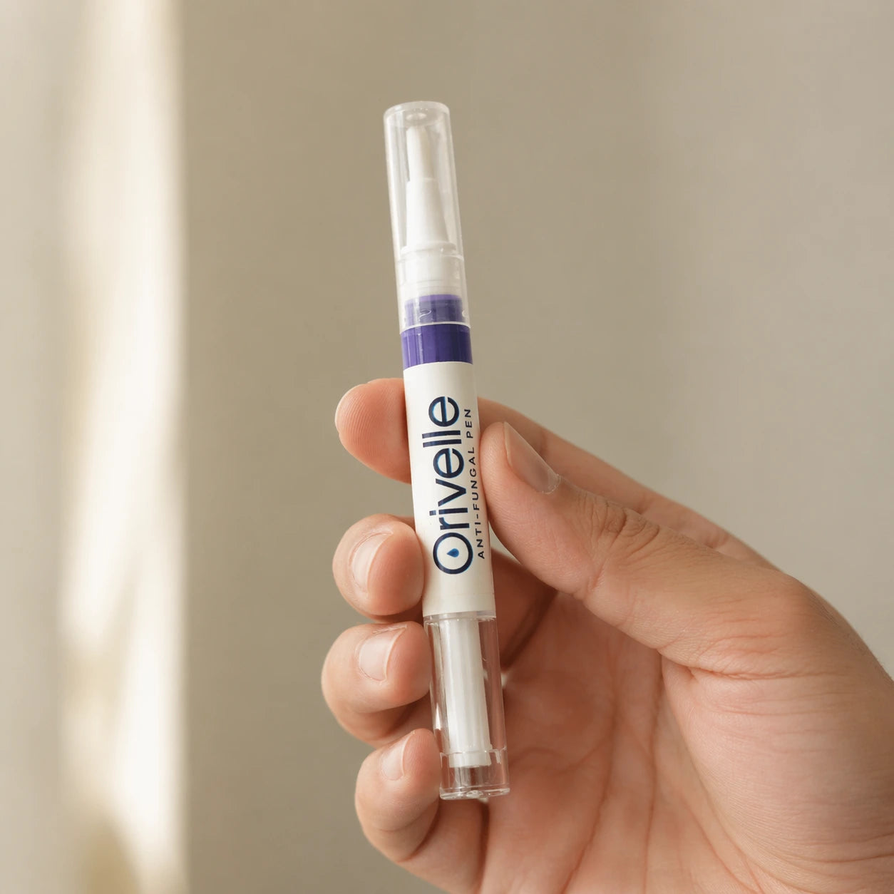 The Orivelle precision applicator pen held between thumb and index finger, showing its palm-sized scale and fine ceramic tip.