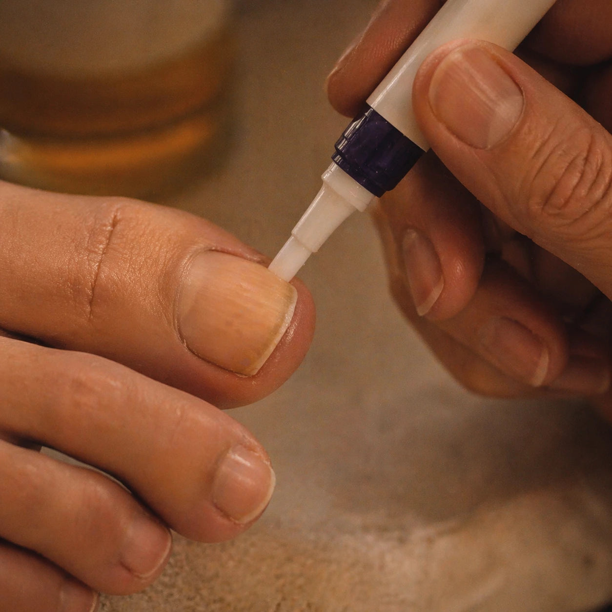 Close-up of the Orivelle ceramic tip being drawn along a toenail cuticle in warm evening bathroom light.