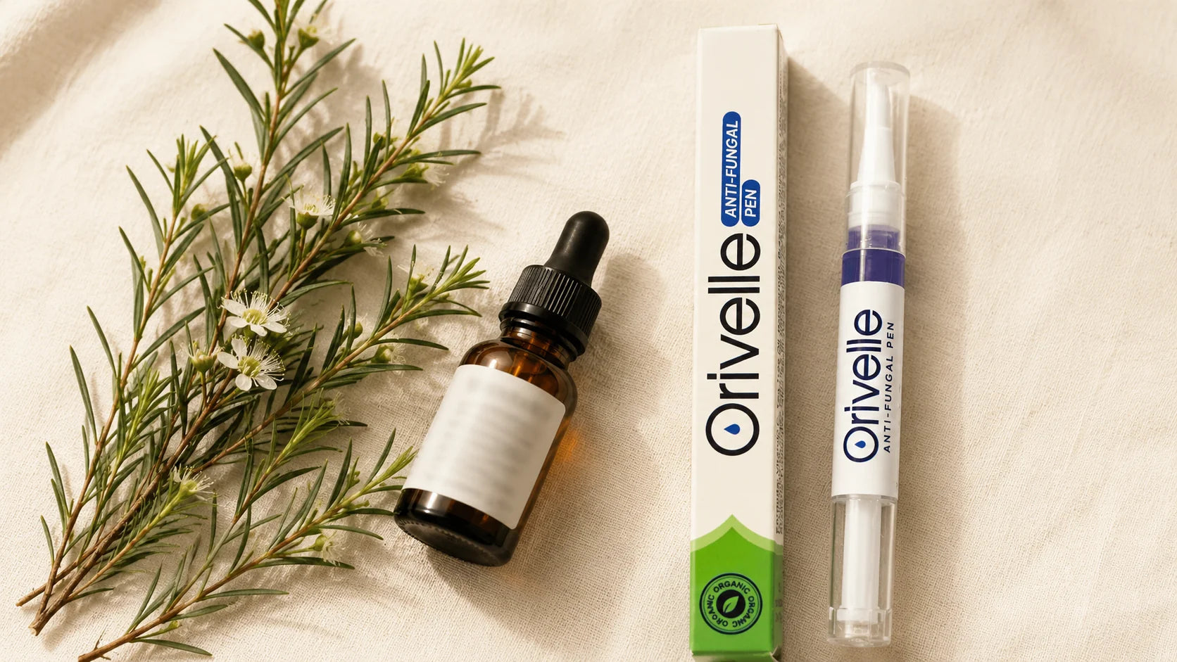 Editorial flat-lay hero showing fresh tea tree leaves and a small amber dropper bottle of essential oil beside the Orivelle pen and box on a warm cream linen surface, soft natural daylight.