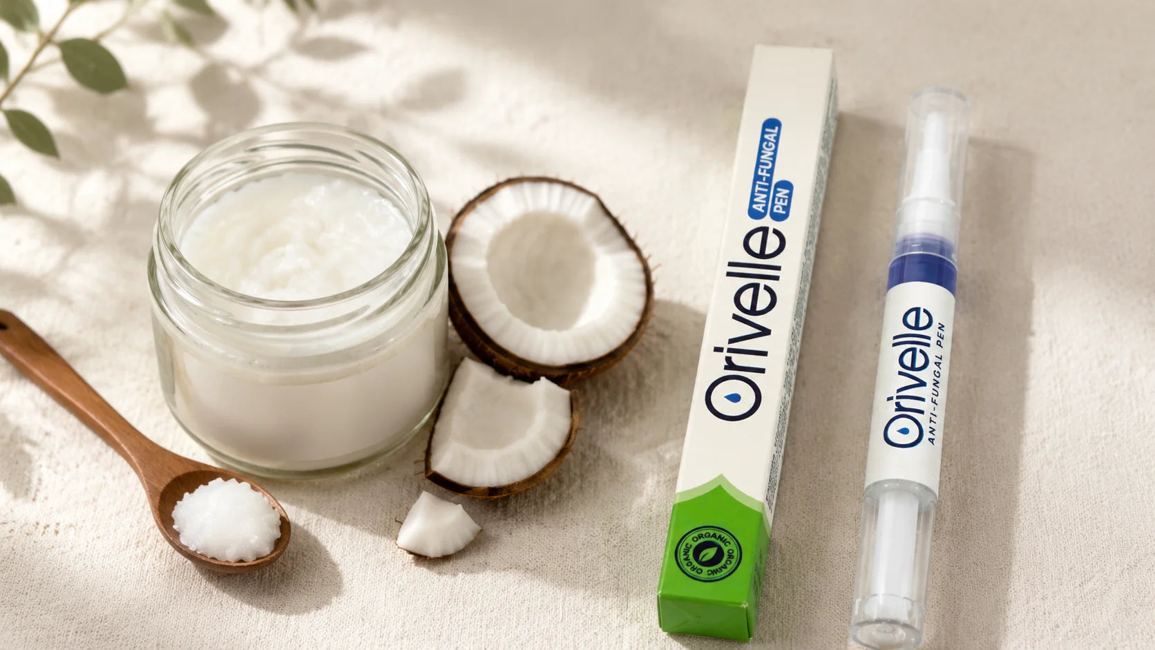 Editorial flat-lay hero showing a small open jar of coconut oil with a wooden spoon, fresh coconut halves, and the Orivelle anti-fungal pen on a warm cream linen surface, soft natural daylight.